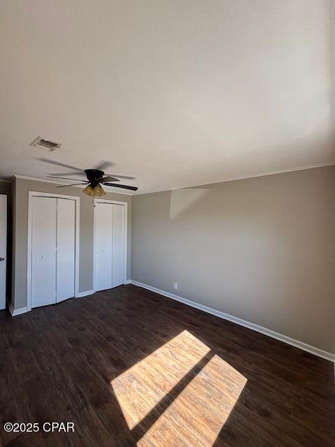 unfurnished bedroom featuring baseboards, visible vents, a ceiling fan, dark wood-type flooring, and two closets