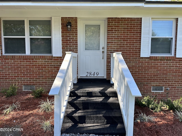 view of exterior entry with crawl space and brick siding