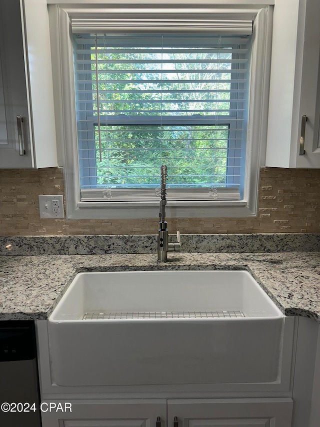 interior details featuring dishwasher, sink, light stone counters, backsplash, and white cabinets