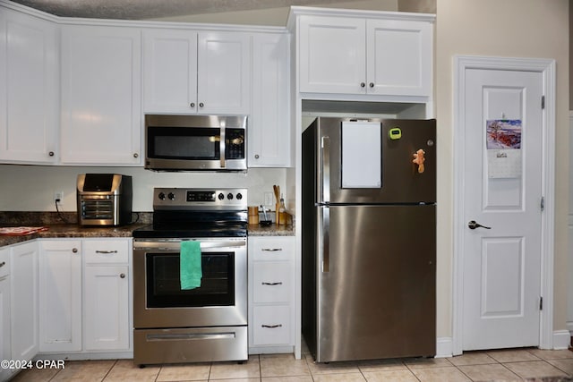 kitchen featuring dark stone counters, a textured ceiling, light tile patterned flooring, white cabinetry, and appliances with stainless steel finishes