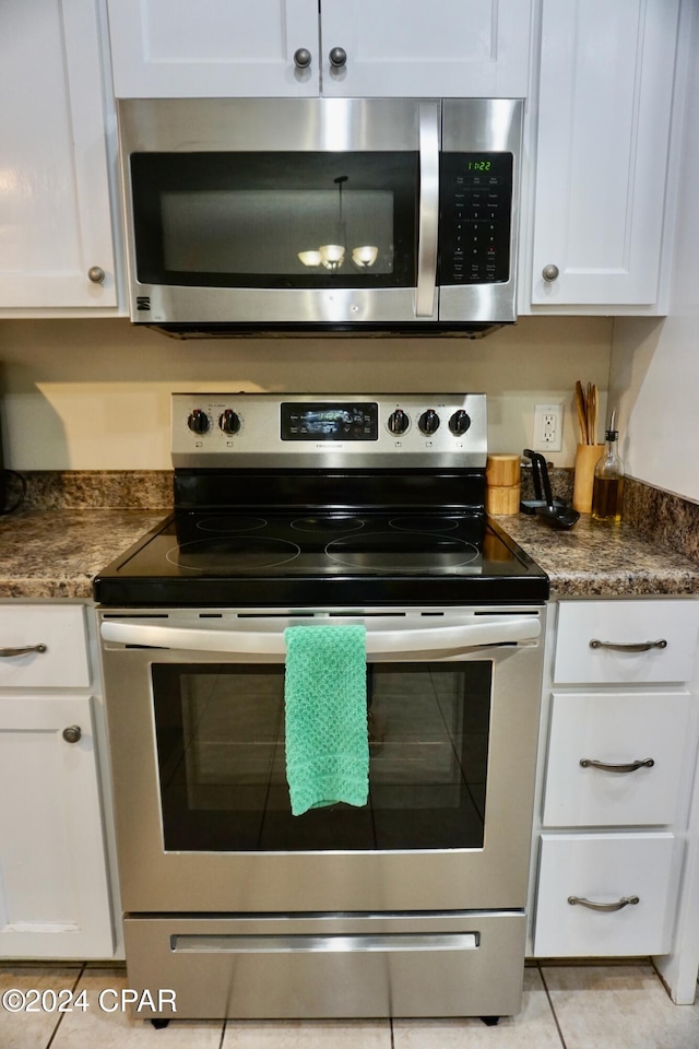 kitchen with white cabinetry, appliances with stainless steel finishes, dark stone counters, and light tile patterned floors