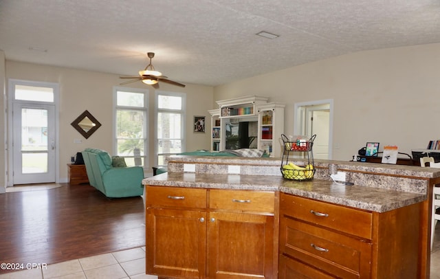 kitchen with a center island, a textured ceiling, ceiling fan, a fireplace, and light hardwood / wood-style flooring