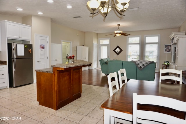 kitchen with white cabinets, stainless steel fridge, light tile patterned floors, and ceiling fan with notable chandelier