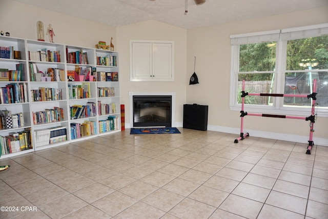 living area with ceiling fan, a textured ceiling, light tile patterned floors, and vaulted ceiling