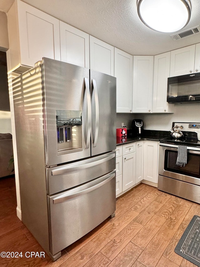 kitchen featuring white cabinetry, light hardwood / wood-style flooring, stainless steel appliances, and a textured ceiling