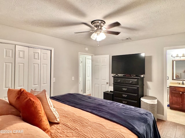 bedroom featuring ceiling fan, light hardwood / wood-style floors, a textured ceiling, and ensuite bath