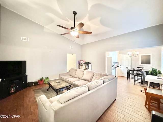 living room with ceiling fan with notable chandelier, light hardwood / wood-style floors, and high vaulted ceiling