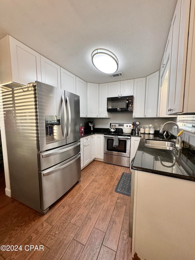 kitchen with white cabinets, sink, a textured ceiling, light hardwood / wood-style floors, and stainless steel appliances