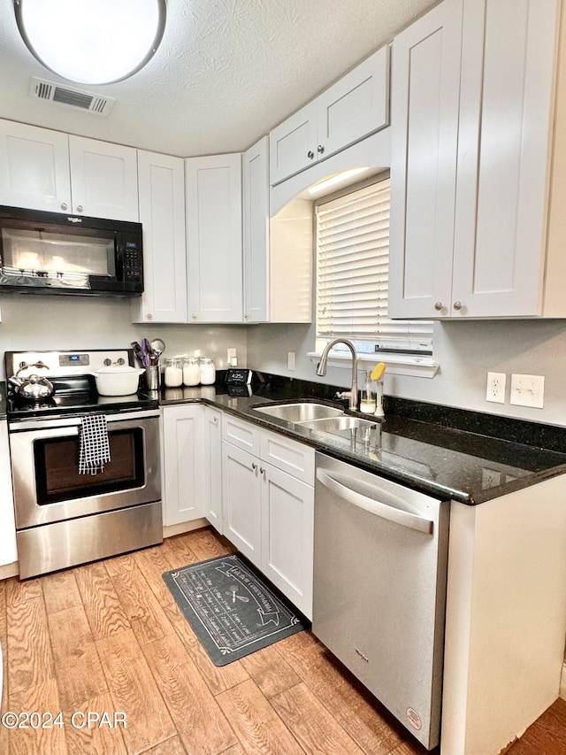 kitchen featuring dark stone counters, stainless steel appliances, sink, light hardwood / wood-style flooring, and white cabinets