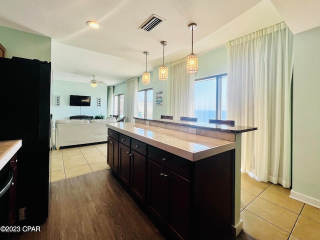 kitchen with light hardwood / wood-style floors, black refrigerator, dark brown cabinets, a kitchen island, and pendant lighting