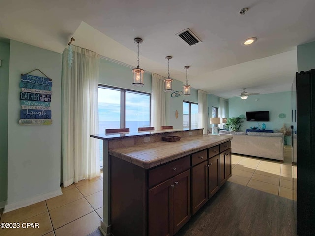 kitchen with dark brown cabinetry, ceiling fan, tile counters, pendant lighting, and light hardwood / wood-style floors