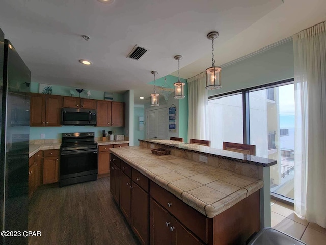 kitchen featuring dark hardwood / wood-style flooring, a kitchen island, black appliances, and decorative light fixtures