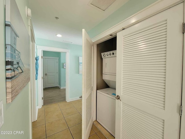 laundry area with stacked washer / drying machine and light tile patterned flooring