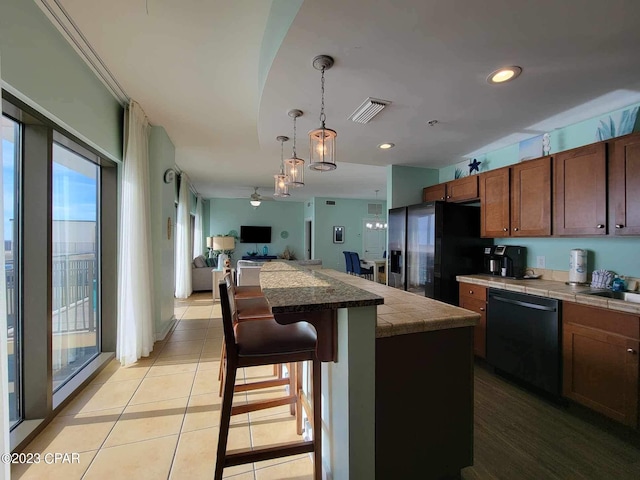 kitchen with a center island, decorative light fixtures, a breakfast bar area, light tile patterned floors, and black appliances