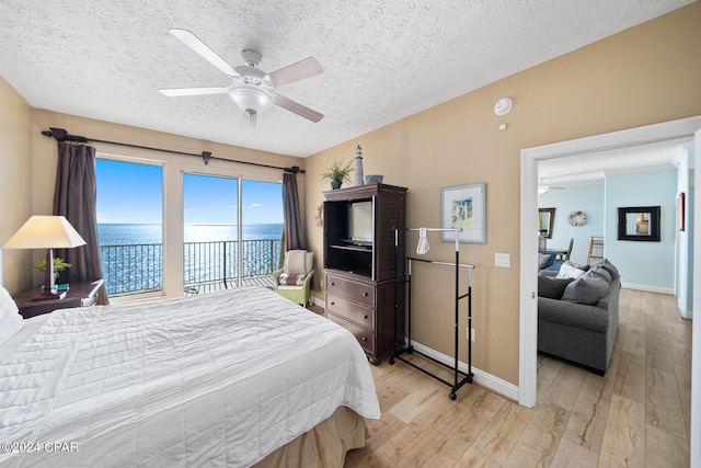 bedroom with a water view, ceiling fan, a textured ceiling, access to exterior, and light wood-type flooring