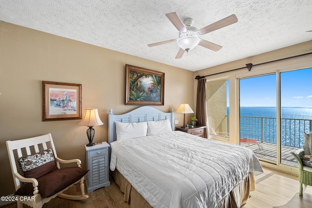 8715 Surf Dr Unit 1402B, Panama City, FL 32408 - bedroom with a textured ceiling, access to outside, a water view, wood finished floors, and a ceiling fan