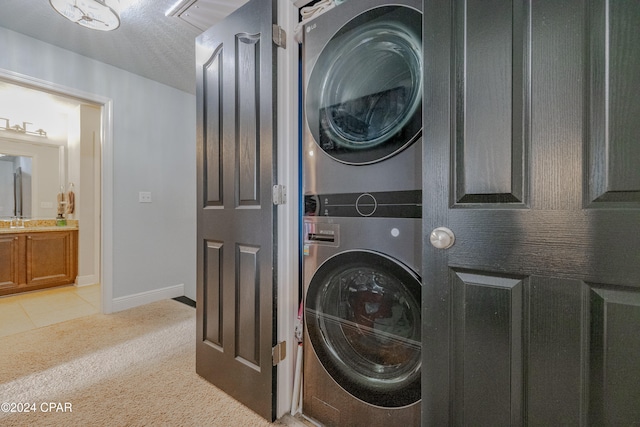 washroom featuring sink, light colored carpet, stacked washing maching and dryer, and a textured ceiling