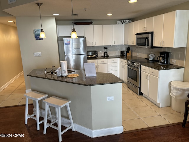 kitchen with tasteful backsplash, stainless steel appliances, white cabinets, light hardwood / wood-style floors, and hanging light fixtures