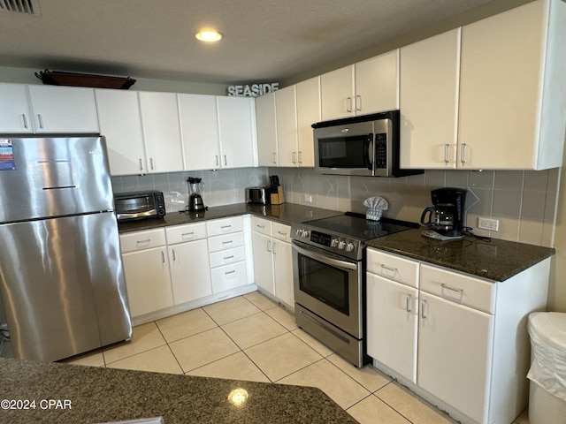 kitchen featuring decorative backsplash, dark stone counters, stainless steel appliances, light tile patterned floors, and white cabinetry