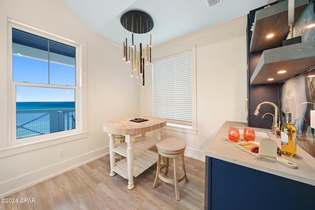 dining room with light hardwood / wood-style flooring, a water view, a healthy amount of sunlight, and vaulted ceiling