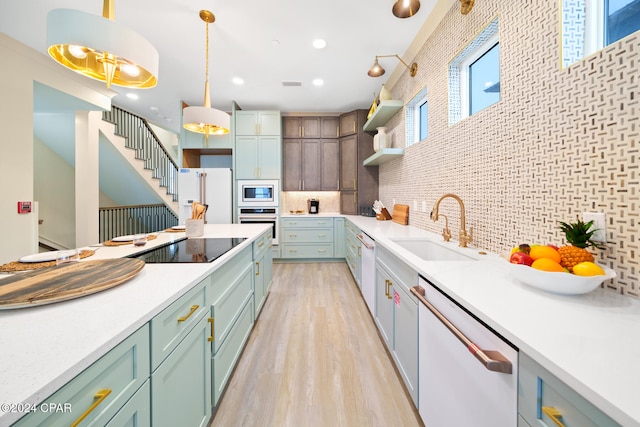 kitchen with stainless steel appliances, decorative backsplash, hanging light fixtures, sink, and light wood-type flooring