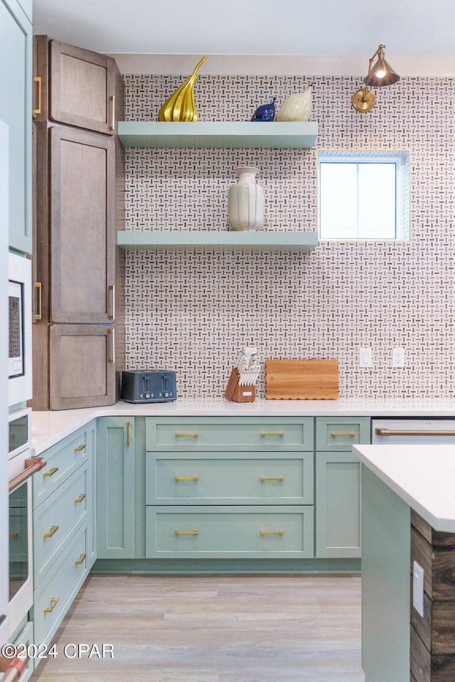 kitchen with green cabinets, light wood-type flooring, decorative backsplash, and oven