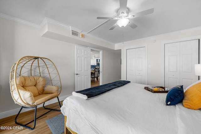 bedroom with hardwood / wood-style floors, crown molding, ceiling fan, and multiple closets