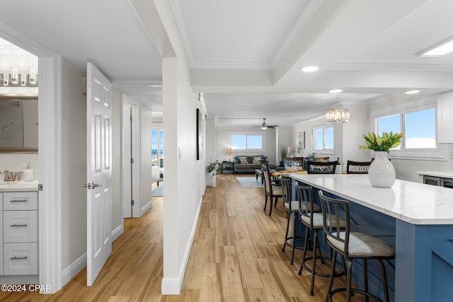 kitchen featuring ceiling fan with notable chandelier, crown molding, light hardwood / wood-style flooring, light stone counters, and a kitchen bar