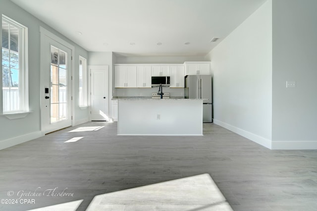 kitchen with a kitchen island with sink, white cabinets, light hardwood / wood-style floors, light stone counters, and stainless steel appliances