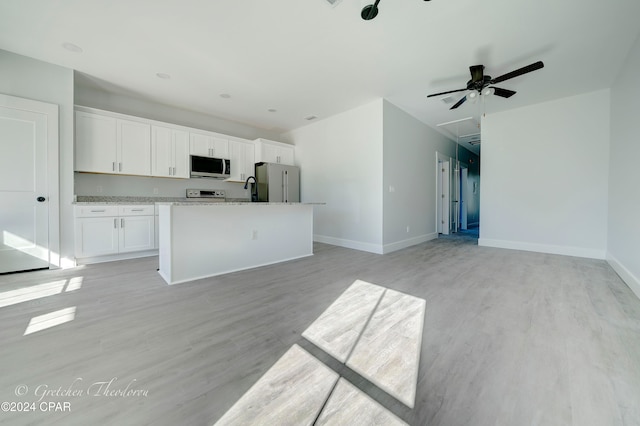 kitchen with white cabinets, a center island with sink, light wood-type flooring, light stone counters, and stainless steel appliances