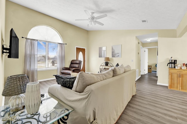 living room with ceiling fan, vaulted ceiling, light hardwood / wood-style flooring, and a textured ceiling