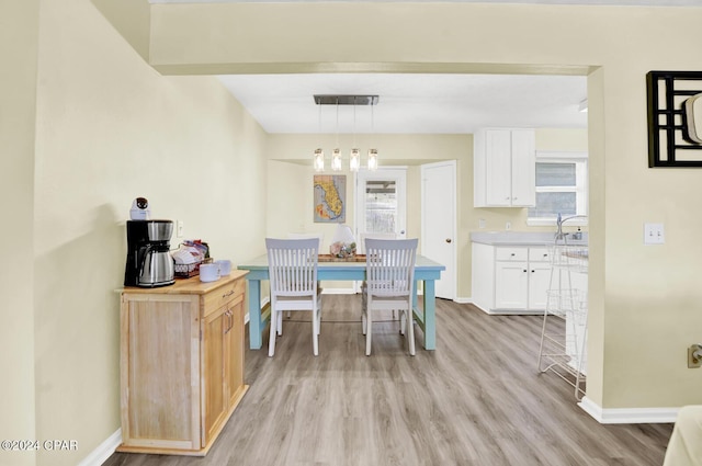 kitchen with wooden counters, a healthy amount of sunlight, white cabinets, decorative light fixtures, and light wood-type flooring