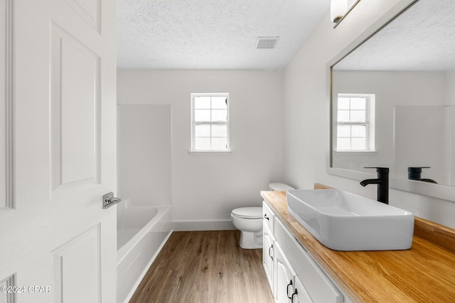 full bathroom with vanity, wood-type flooring, a healthy amount of sunlight, and a textured ceiling