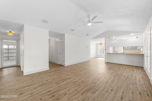 unfurnished living room with ceiling fan, lofted ceiling, a textured ceiling, and light hardwood / wood-style floors