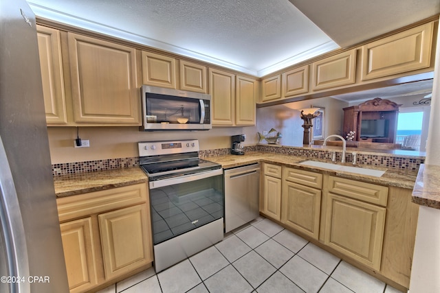 kitchen with appliances with stainless steel finishes, sink, light tile patterned floors, and a textured ceiling