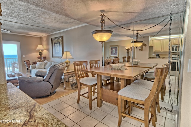 tiled dining space with a water view, ornamental molding, and a textured ceiling