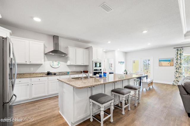 kitchen featuring visible vents, wall chimney range hood, white cabinets, stainless steel appliances, and a sink