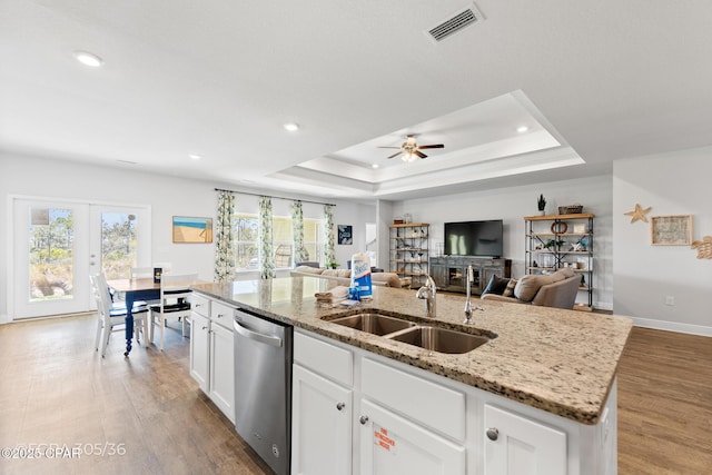 kitchen featuring visible vents, a sink, a tray ceiling, light wood-style floors, and dishwasher