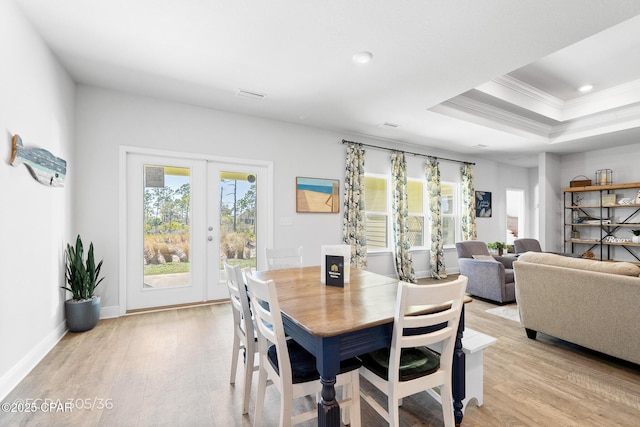 dining area featuring baseboards, a tray ceiling, light wood-style flooring, ornamental molding, and french doors