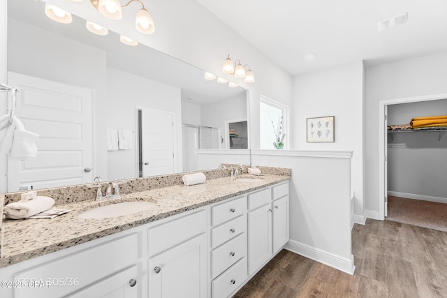 bathroom featuring a spacious closet, baseboards, double vanity, wood finished floors, and a sink