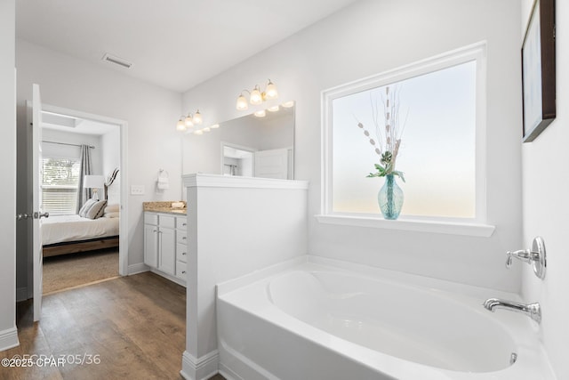 ensuite bathroom with visible vents, ensuite bathroom, wood finished floors, a bath, and vanity