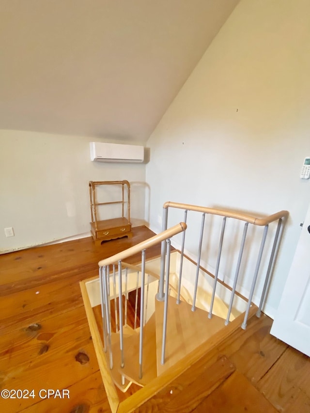 stairway with lofted ceiling, wood-type flooring, and a wall mounted air conditioner