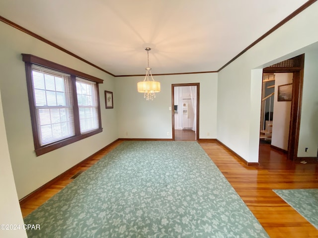 empty room featuring hardwood / wood-style floors, crown molding, and a notable chandelier