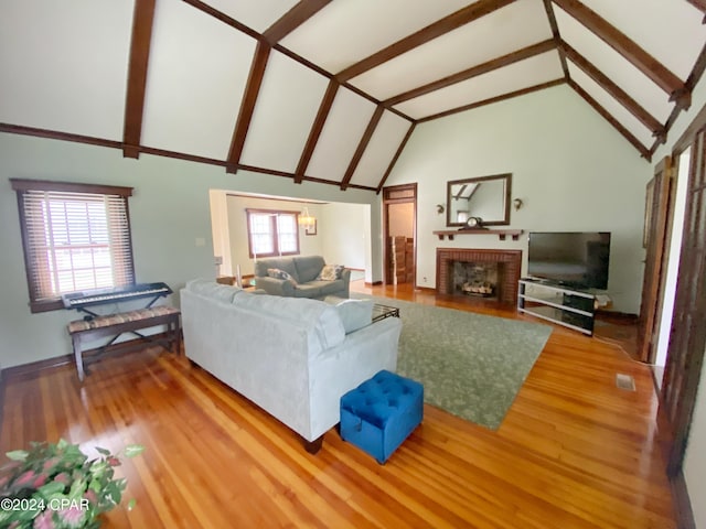 living room with beam ceiling, hardwood / wood-style flooring, a brick fireplace, and plenty of natural light