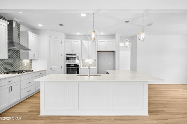 kitchen featuring sink, an island with sink, white cabinets, decorative light fixtures, and wall chimney exhaust hood