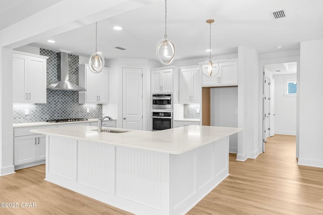 kitchen featuring white cabinetry, a large island with sink, hanging light fixtures, and wall chimney range hood