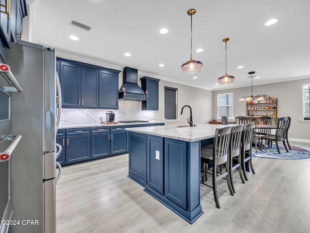 kitchen with premium range hood, a center island with sink, decorative light fixtures, light stone countertops, and light hardwood / wood-style floors