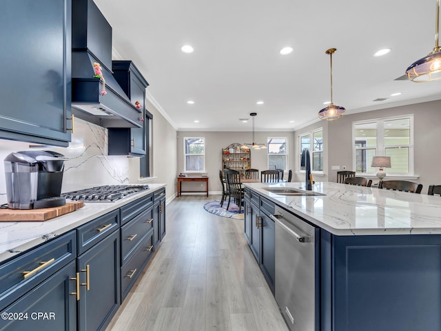 kitchen with a center island with sink, sink, appliances with stainless steel finishes, hanging light fixtures, and light wood-type flooring