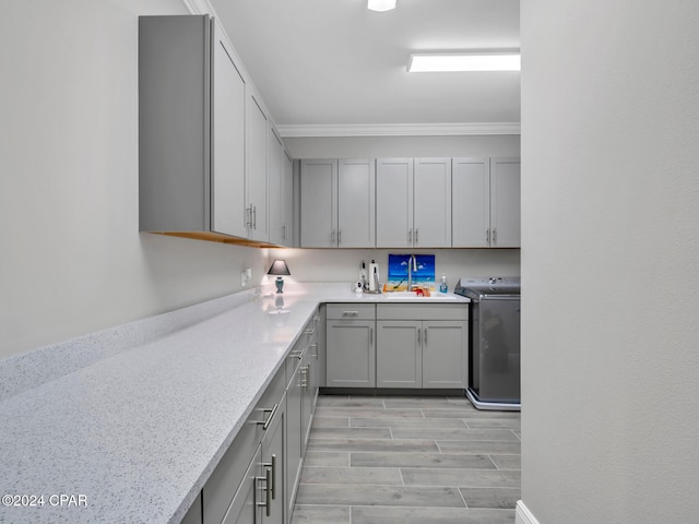 kitchen with gray cabinetry, light stone counters, ornamental molding, washer / dryer, and light wood-type flooring