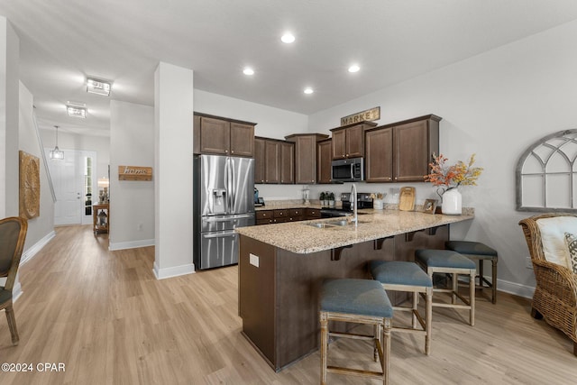 kitchen featuring kitchen peninsula, sink, light stone countertops, light wood-type flooring, and appliances with stainless steel finishes